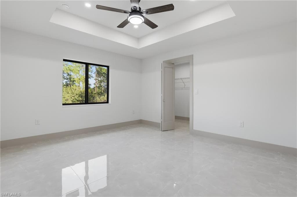Unfurnished bedroom with a spacious closet, a raised ceiling, a ceiling fan, and recessed lighting