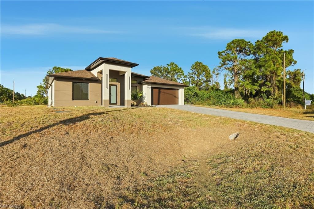 Prairie-style home with driveway, stucco siding, a garage, a front lawn, and roof with shingles