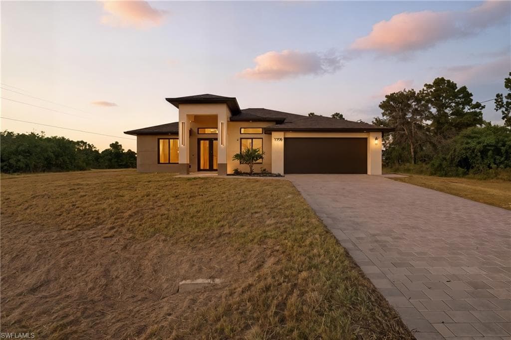 Prairie-style house featuring stucco siding, decorative driveway, an attached garage, and a front yard