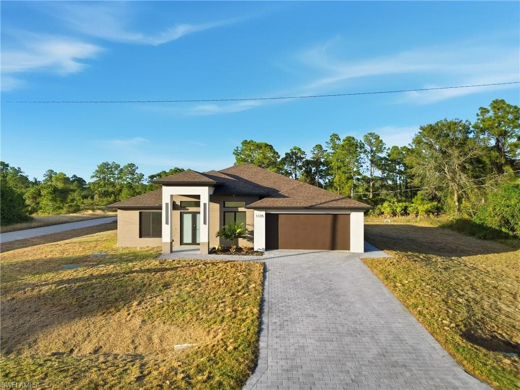 Prairie-style home with decorative driveway, a front lawn, stucco siding, roof with shingles, and an attached garage