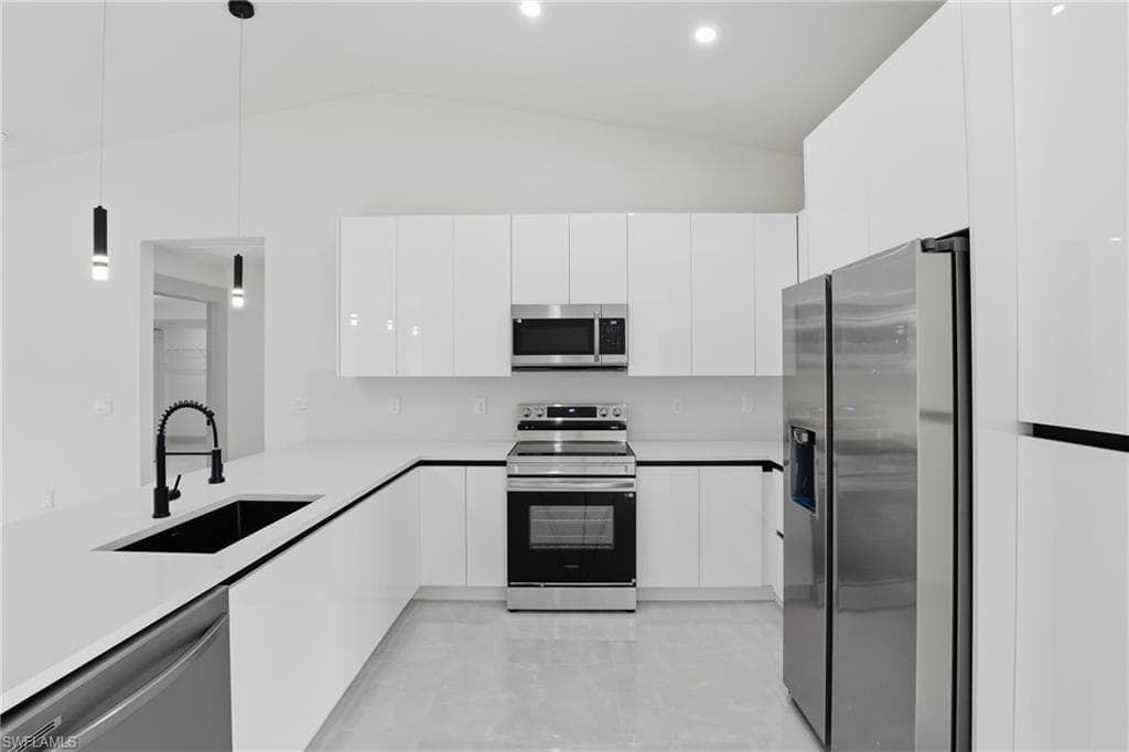 Kitchen with modern cabinets, appliances with stainless steel finishes, decorative light fixtures, white cabinets, and vaulted ceiling