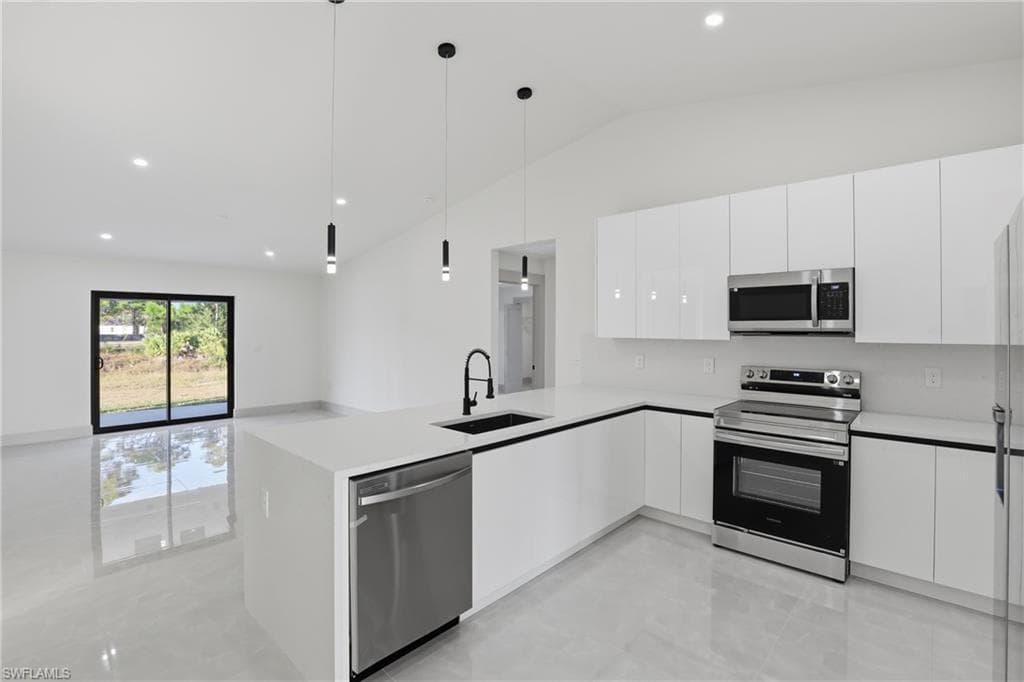 Kitchen with appliances with stainless steel finishes, modern cabinets, hanging light fixtures, lofted ceiling, and a peninsula