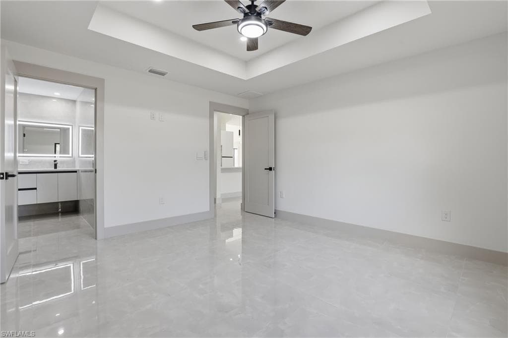 Unfurnished bedroom featuring a tray ceiling, a ceiling fan, and connected bathroom