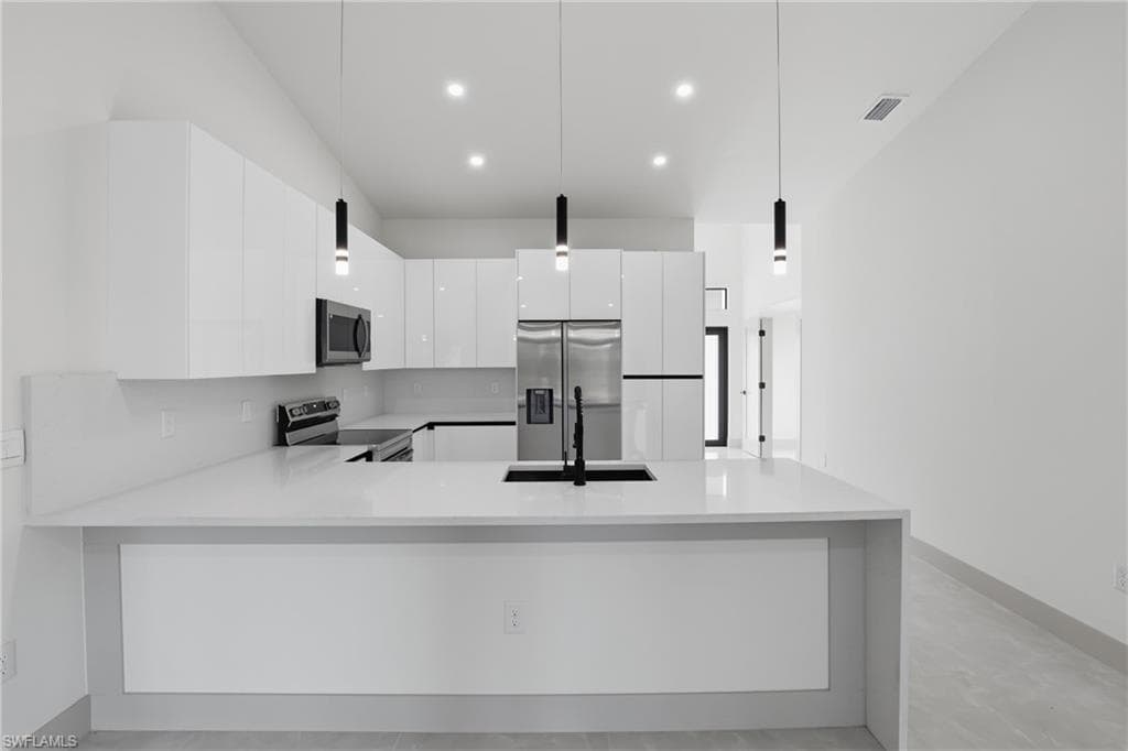 Kitchen featuring modern cabinets, hanging light fixtures, a peninsula, white cabinets, and stainless steel appliances
