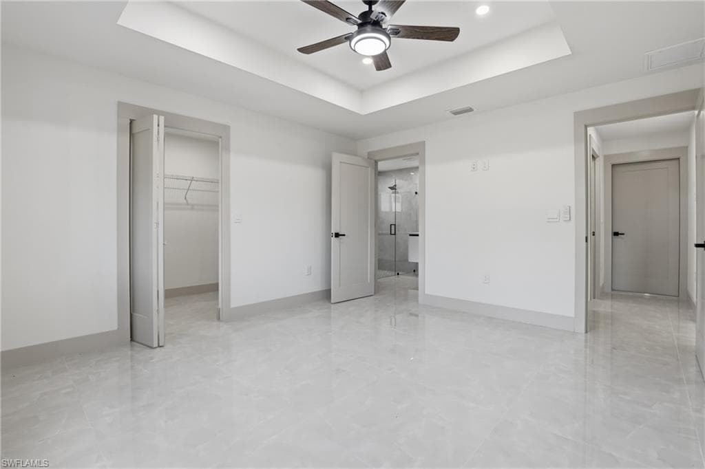 Unfurnished bedroom with a tray ceiling, a spacious closet, ceiling fan, and recessed lighting