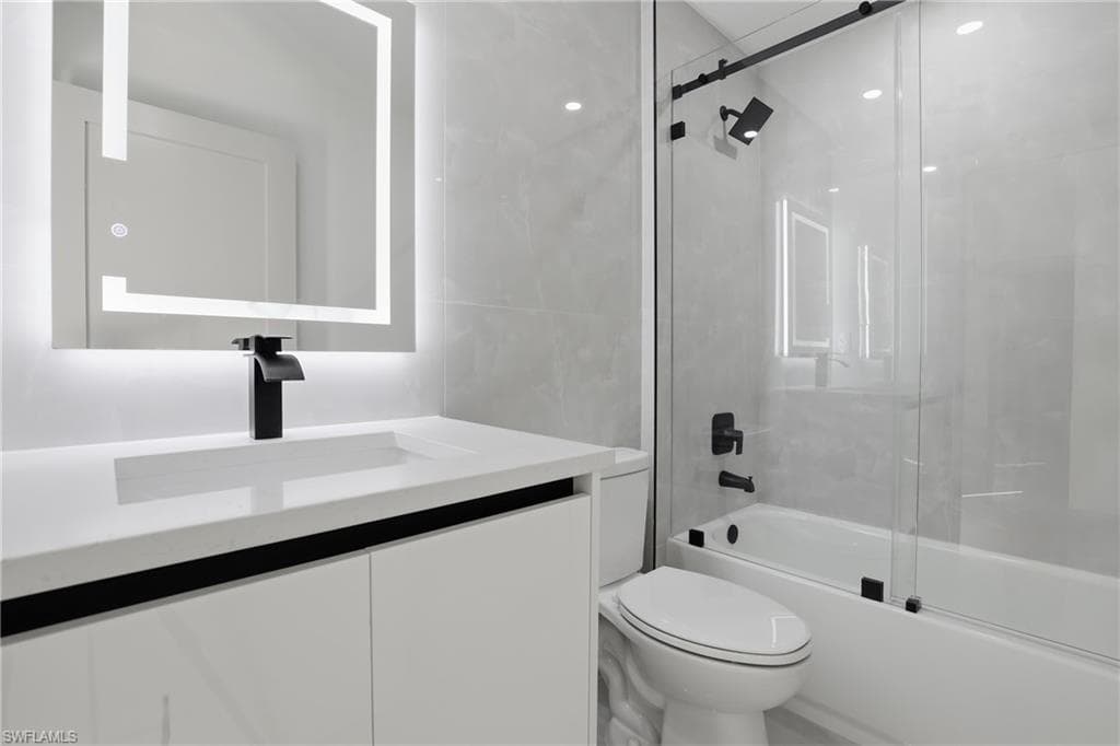 Full bath with shower / bath combination with glass door, vanity, and tile walls
