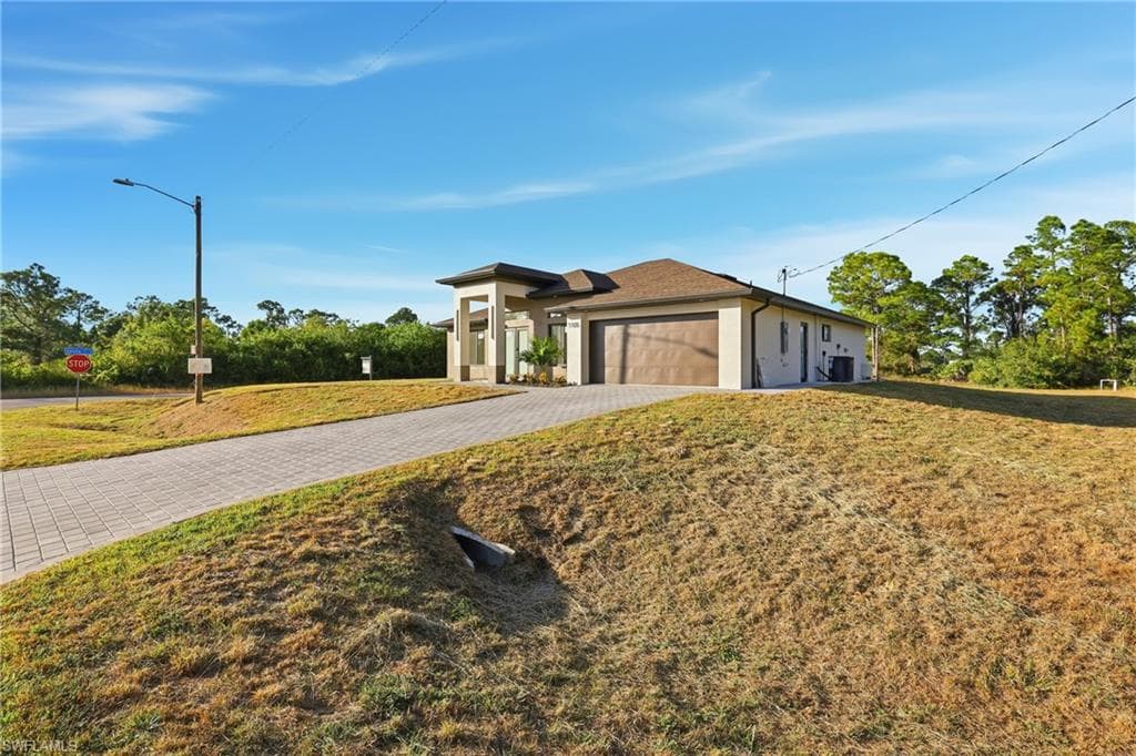 View of front of property with decorative driveway, an attached garage, a front yard, and stucco siding