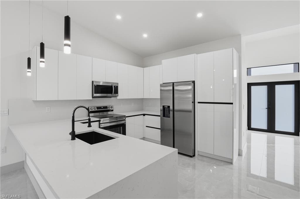 Kitchen with hanging light fixtures, appliances with stainless steel finishes, white cabinets, modern cabinets, and a peninsula