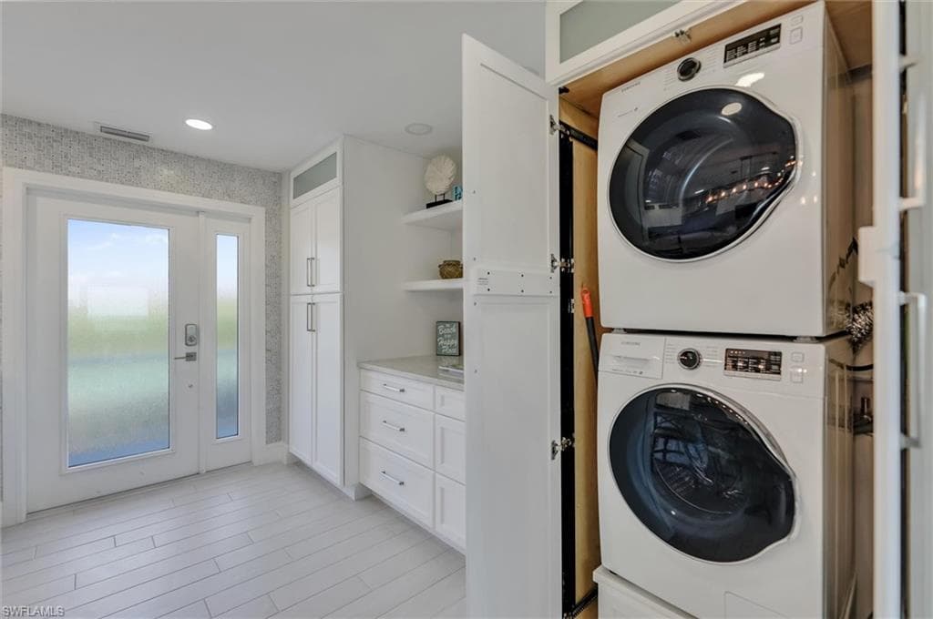 Laundry area featuring stacked washer / drying machine, wallpapered walls, and light wood-type flooring