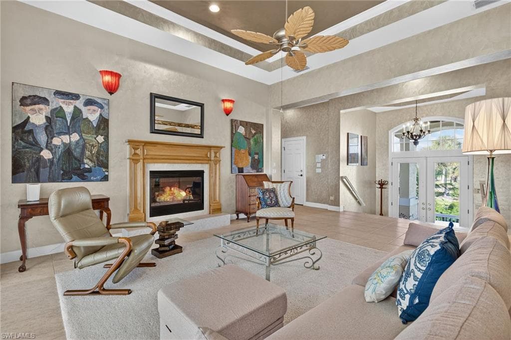 Living room with a tray ceiling, french doors, tile patterned flooring, a premium fireplace, and ceiling fan