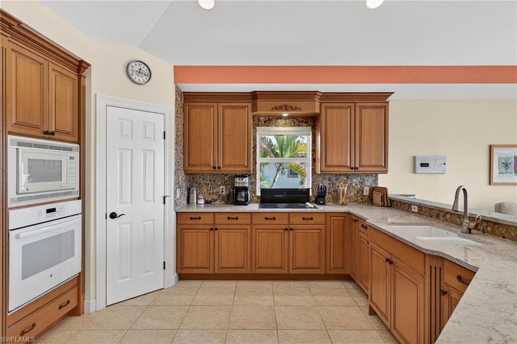Kitchen with brown cabinetry, white appliances, light tile patterned floors, tasteful backsplash, and recessed lighting
