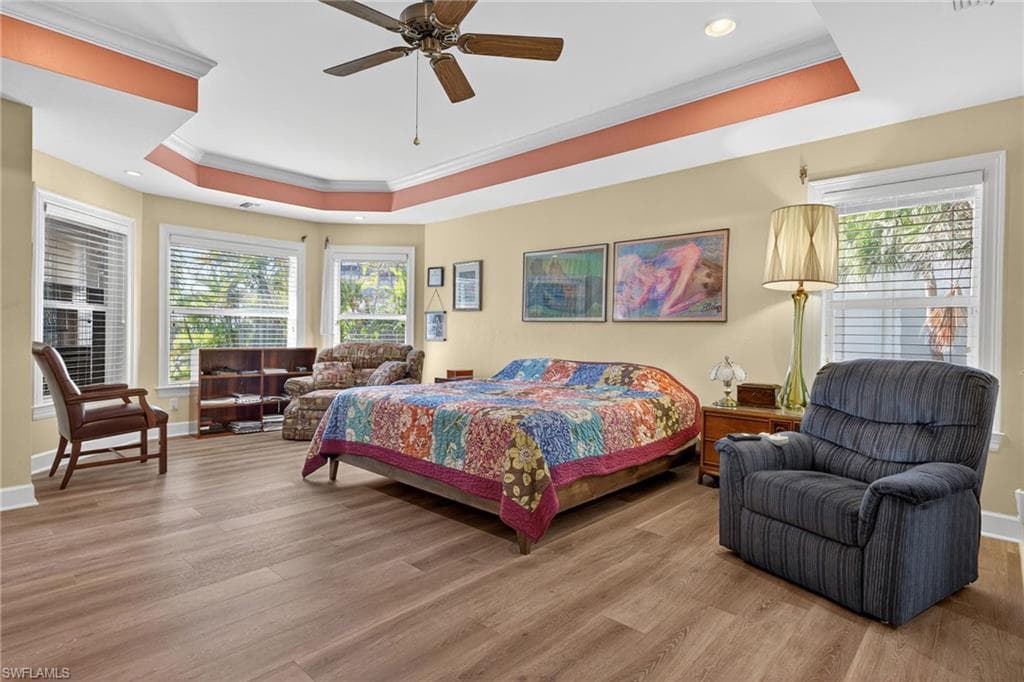 Bedroom featuring a raised ceiling, ornamental molding, light wood-type flooring, ceiling fan, and recessed lighting