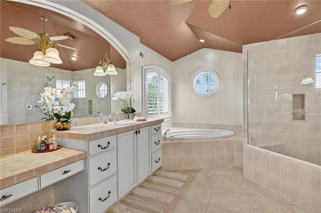 Bathroom featuring ceiling fan, light tile patterned floors, vanity, a walk in shower, and vaulted ceiling