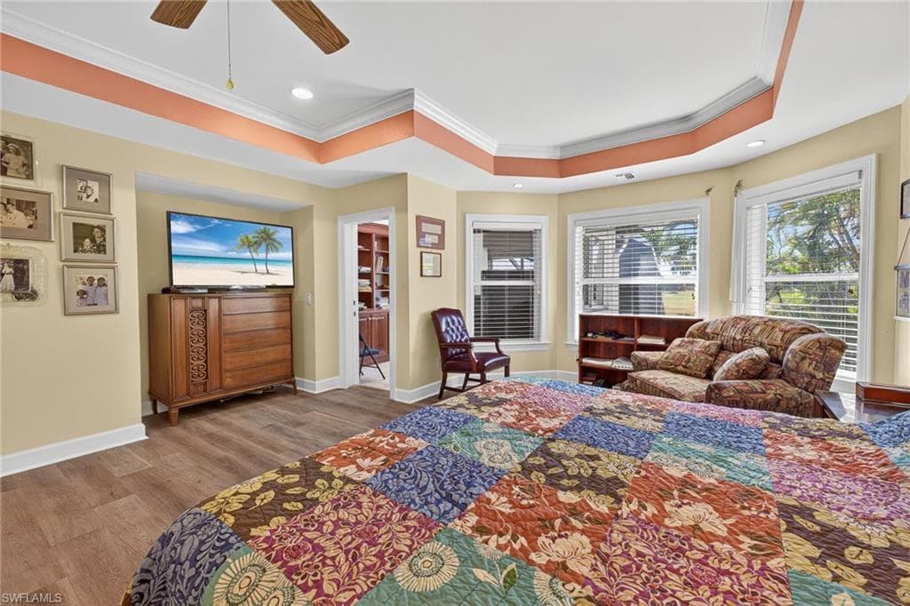 Bedroom featuring wood finished floors, ornamental molding, a ceiling fan, recessed lighting, and a tray ceiling