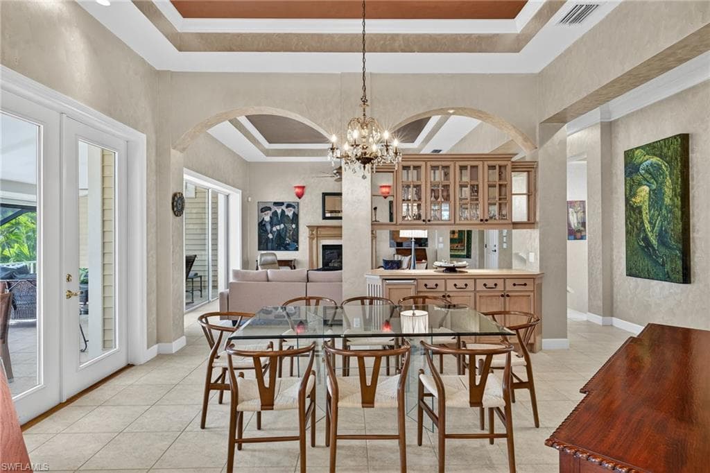 Dining room featuring a tray ceiling, a fireplace, a chandelier, light tile patterned flooring, and arched walkways