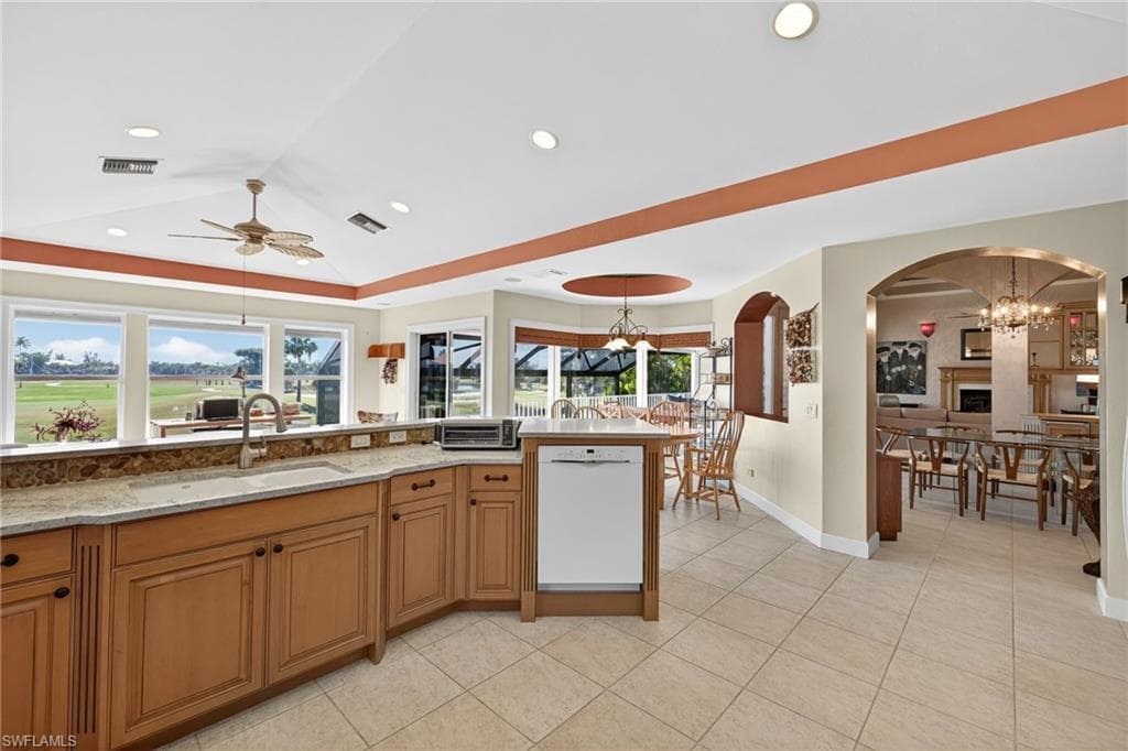 Kitchen with brown cabinets, a chandelier, white dishwasher, a tray ceiling, and light tile patterned floors