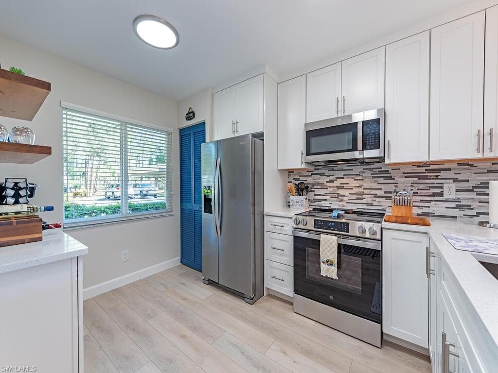 Kitchen featuring appliances with stainless steel finishes, white cabinets, light stone counters, light wood-type flooring, and decorative backsplash