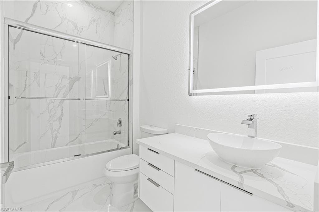 Full bathroom with vanity, light marble finish flooring, shower / bath combination with glass door, and a textured wall