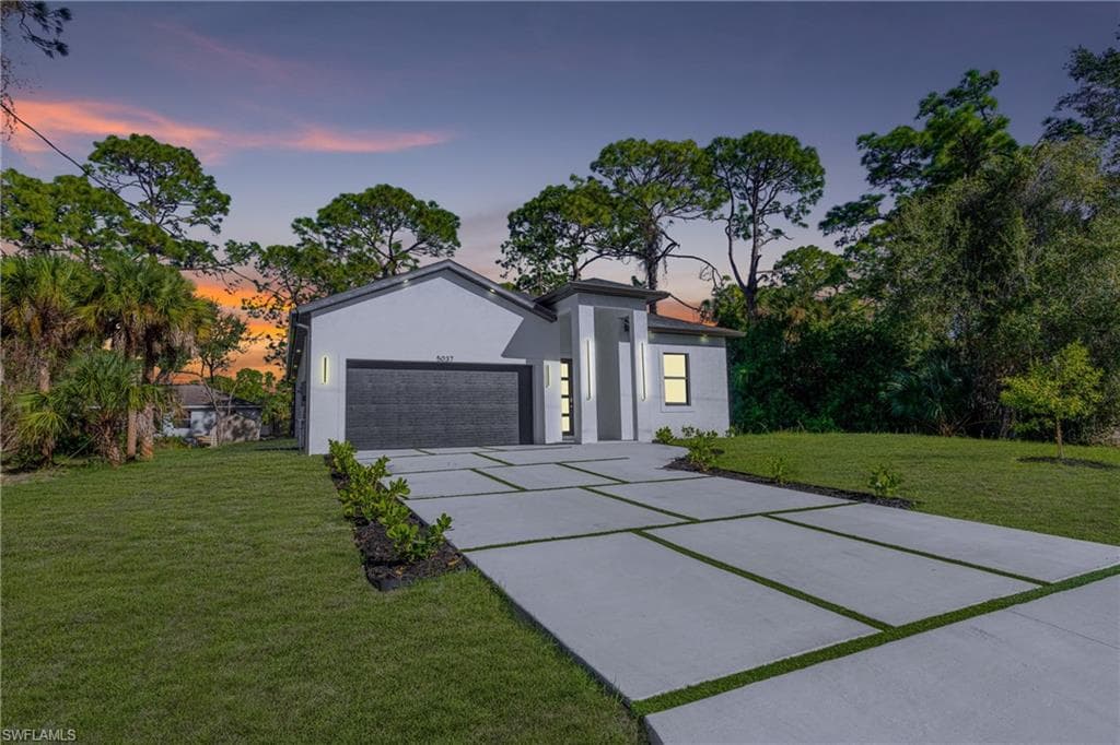 View of front of house featuring stucco siding, an attached garage, a front lawn, and concrete driveway