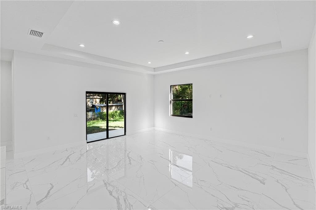 Unfurnished room with light marble finish flooring, recessed lighting, and a tray ceiling