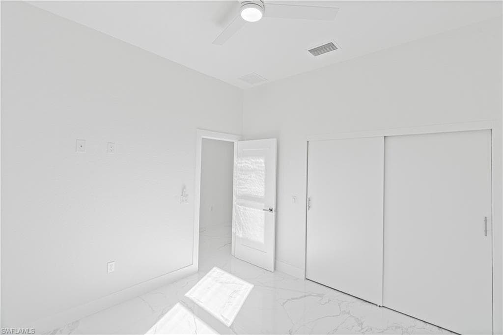 Unfurnished bedroom featuring light marble finish flooring, ceiling fan, and a closet