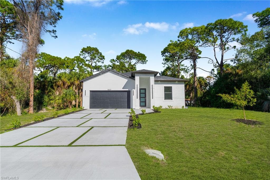 View of front of home featuring stucco siding, concrete driveway, a front yard, a garage, and view of scattered trees
