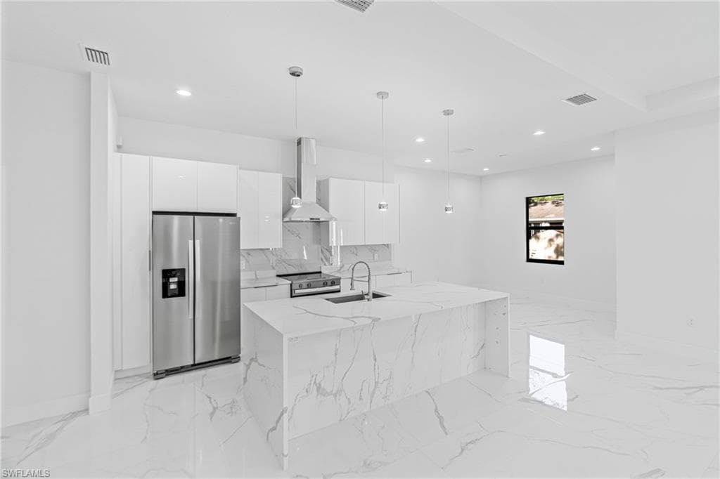 Kitchen with appliances with stainless steel finishes, white cabinetry, wall chimney exhaust hood, modern cabinets, and pendant lighting
