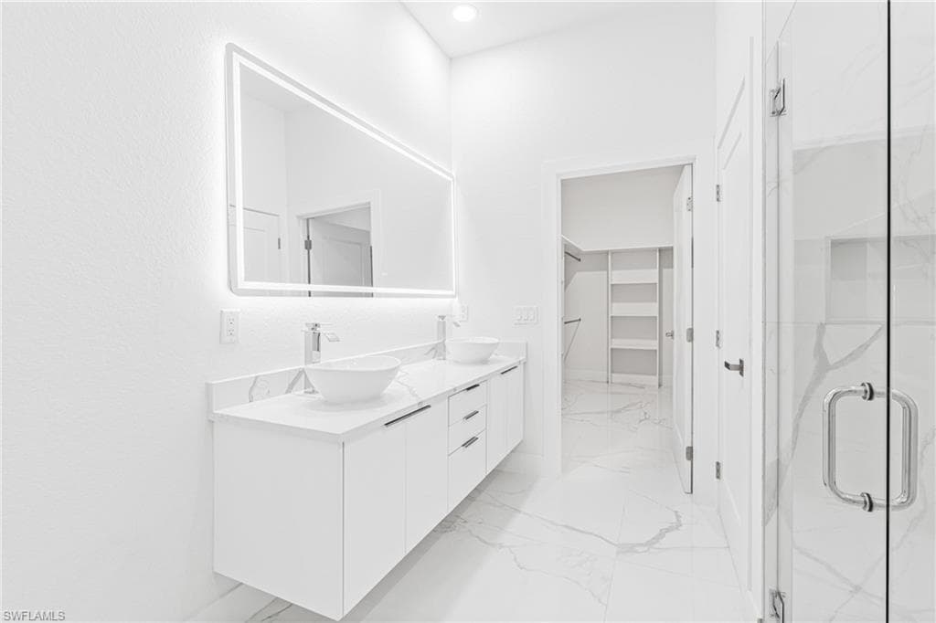 Bathroom featuring double vanity, light marble finish flooring, a marble finish shower, and a spacious closet
