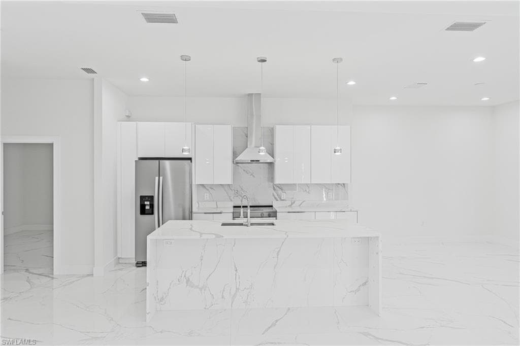 Kitchen featuring modern cabinets, stainless steel appliances, wall chimney range hood, pendant lighting, and white cabinets