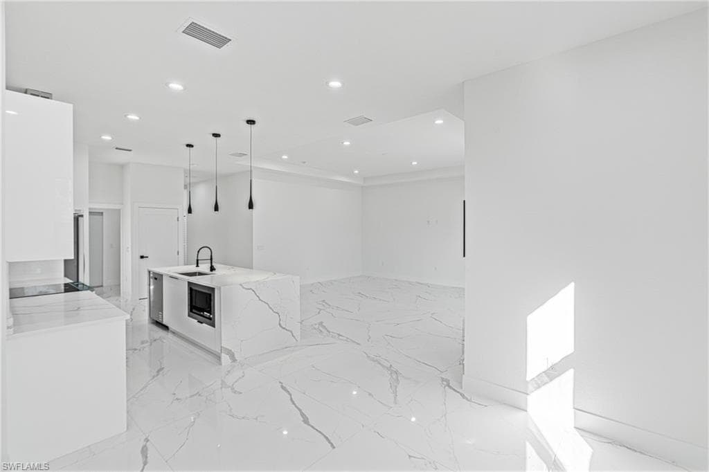 Kitchen featuring recessed lighting, light stone countertops, white cabinetry, decorative light fixtures, and an island with sink