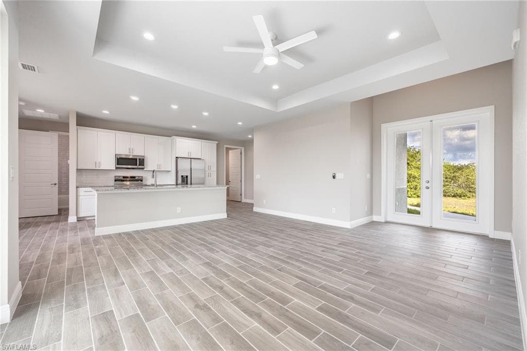Unfurnished living room with a ceiling fan, wood tiled floors, recessed lighting, french doors, and a tray ceiling-Finishes may vary