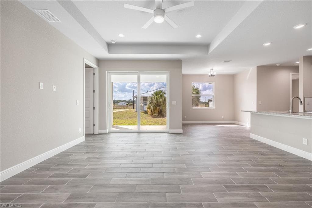 Unfurnished living room featuring ceiling fan, wood finish floors, a tray ceiling, and recessed lighting-Finishes may vary