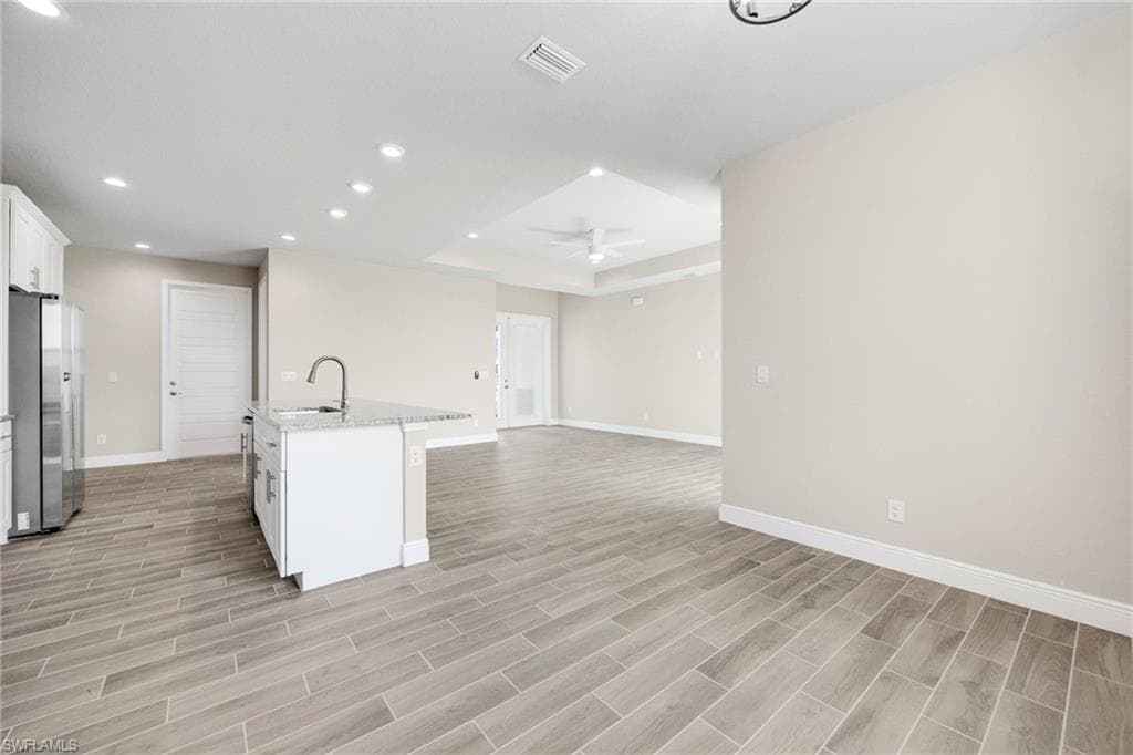 Kitchen featuring white cabinetry, an island with sink, light stone counters, freestanding refrigerator, and open floor plan-Finishes may vary