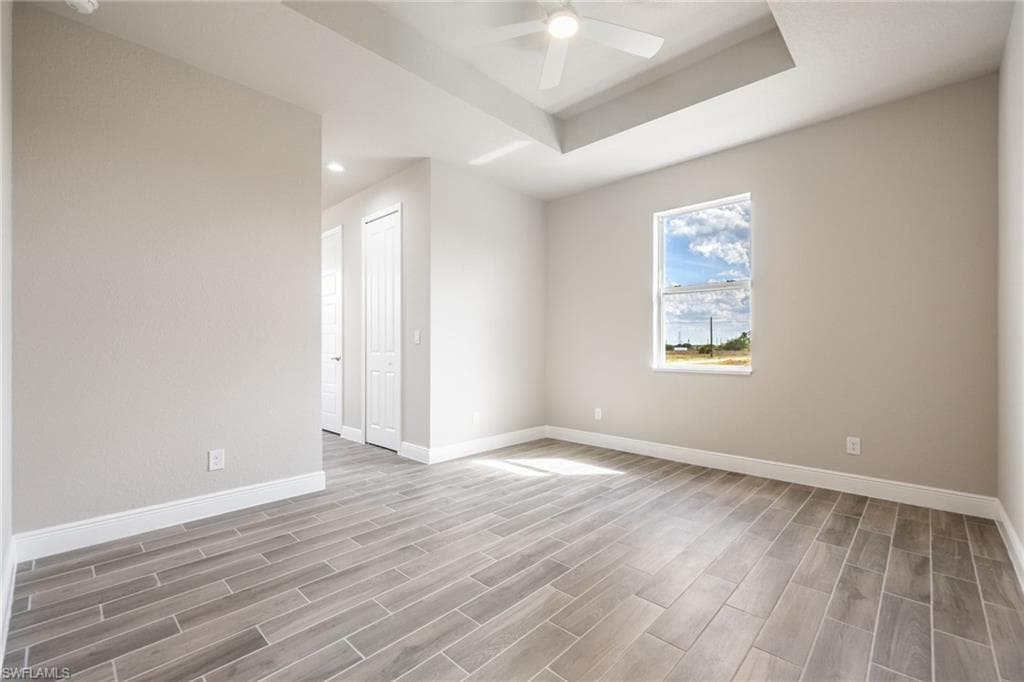 Empty room with wood finish floors, a tray ceiling, and ceiling fan-Finishes may vary