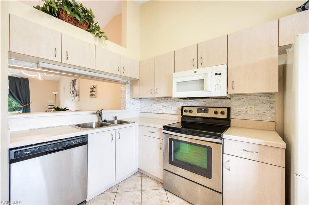 Kitchen featuring stainless steel appliances, light countertops, backsplash, a high ceiling, and light tile patterned floors