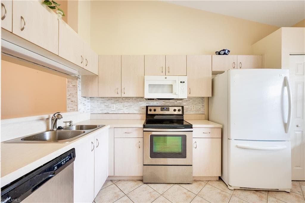 Kitchen featuring appliances with stainless steel finishes, light countertops, decorative backsplash, light tile patterned flooring, and light brown cabinets