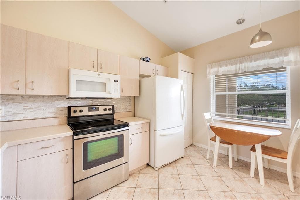 Kitchen featuring white appliances, light countertops, tasteful backsplash, hanging light fixtures, and vaulted ceiling