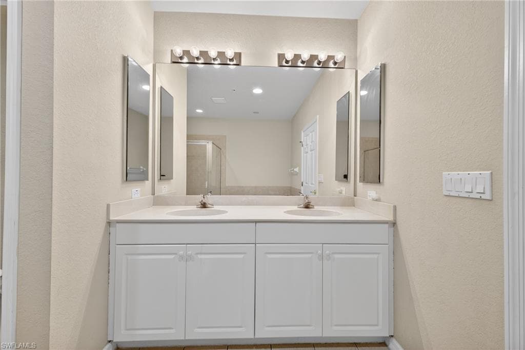 Bathroom featuring a textured wall, double vanity, and a shower stall
