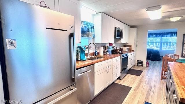 Kitchen featuring stainless steel appliances, butcher block countertops, white cabinetry, and light wood-type flooring