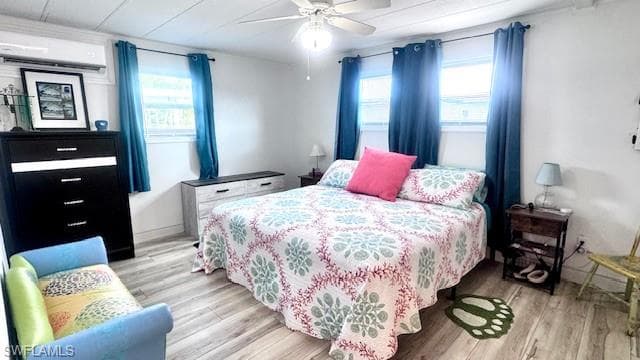 Bedroom featuring light wood finished floors, a wall mounted AC, multiple windows, and ceiling fan