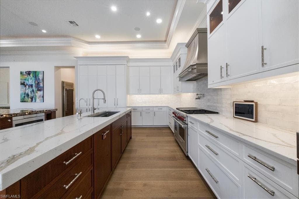 Kitchen with glass insert cabinets, appliances with stainless steel finishes, white cabinetry, a kitchen island with sink, and crown molding