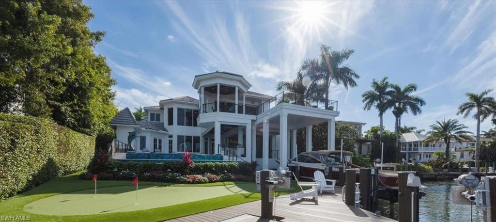 Rear view of house with an area to practice putting, a balcony, boat lift, a water view, and a patio