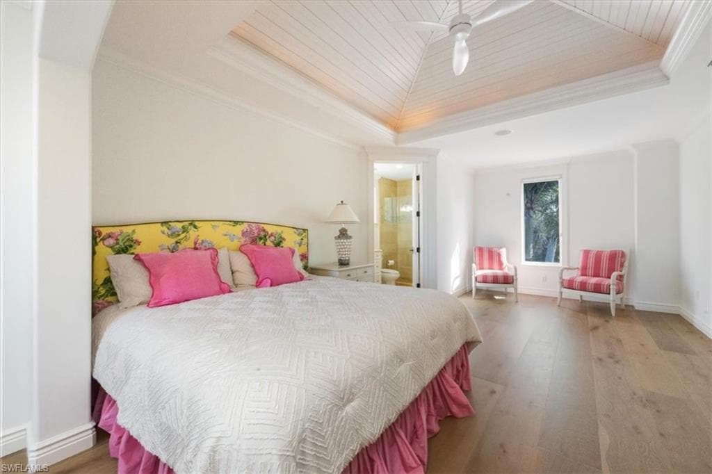 Bedroom featuring wood-type flooring, ornamental molding, connected bathroom, a ceiling fan, and a tray ceiling