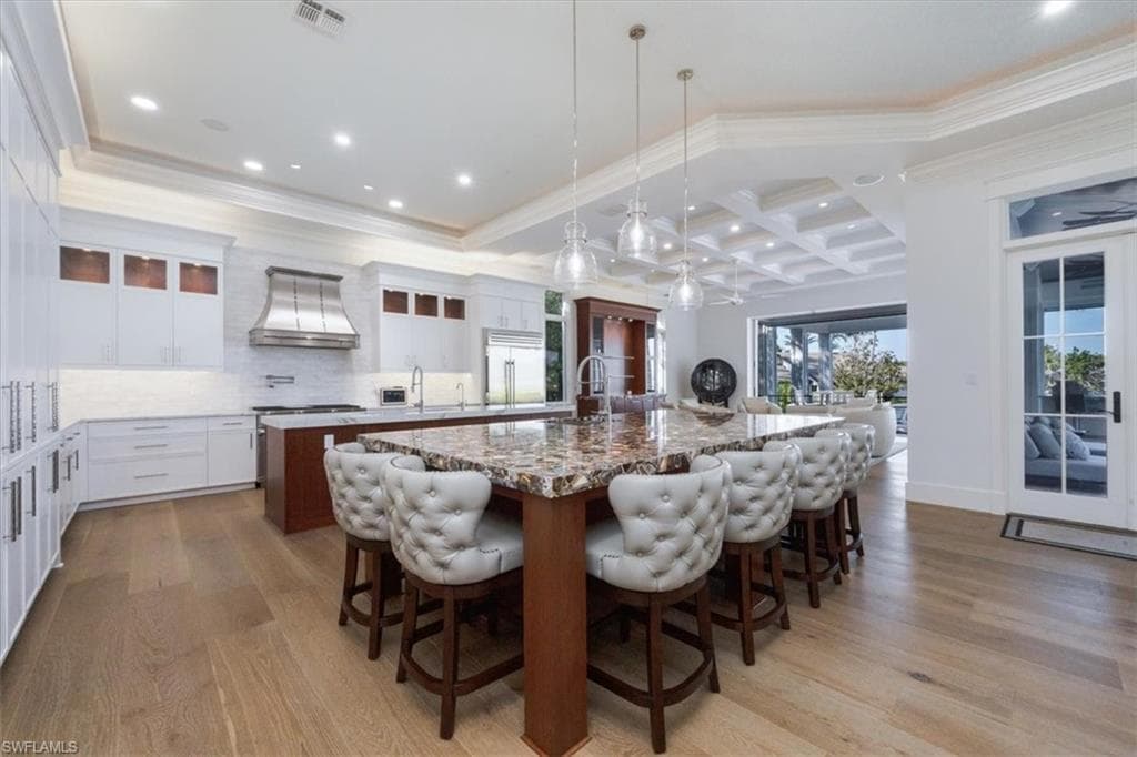 Kitchen with decorative light fixtures, glass insert cabinets, white cabinetry, coffered ceiling, and light wood-style flooring