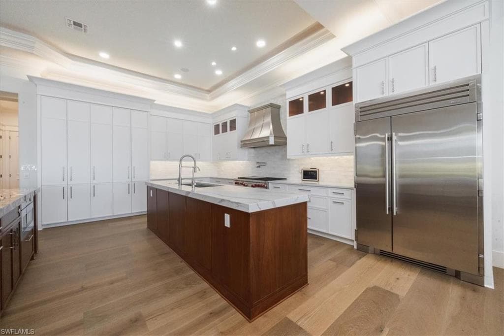 Kitchen with glass insert cabinets, appliances with stainless steel finishes, white cabinetry, a kitchen island with sink, and crown molding