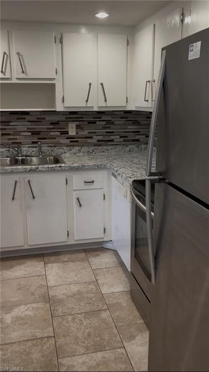 Kitchen with appliances with stainless steel finishes, white cabinets, backsplash, and light tile patterned floors