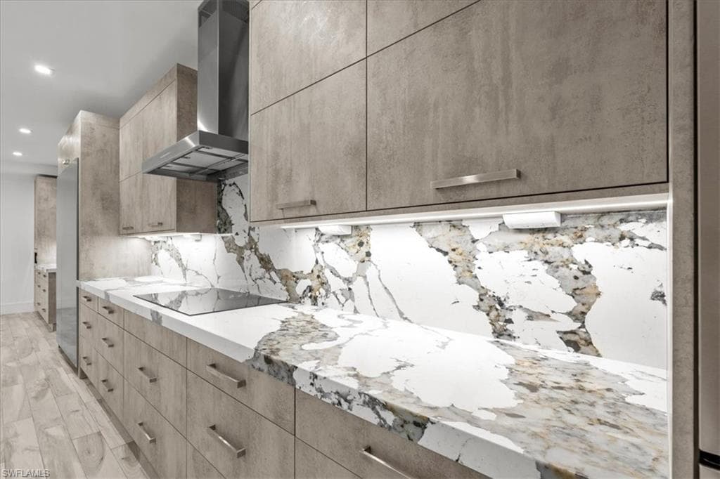 Kitchen featuring modern cabinets, light brown cabinetry, recessed lighting, wall chimney exhaust hood, and light stone counters