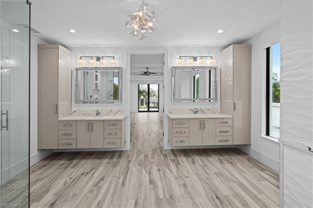 Bathroom with two vanities, light wood-style flooring, a chandelier, and a shower stall