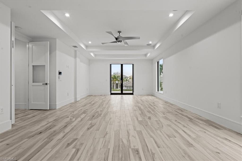 Unfurnished living room with light wood-style floors, recessed lighting, a raised ceiling, and a ceiling fan