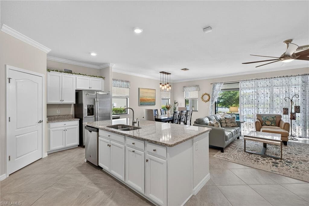 Kitchen with white cabinetry, decorative light fixtures, crown molding, light stone countertops, and plenty of natural light